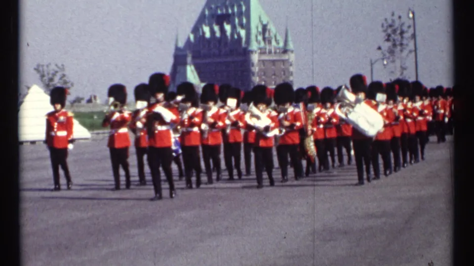 The Ottawa parade formation stretches across the frame as red-uniformed brass musicians march on a wide paved route.