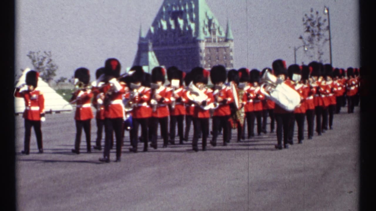 Red-uniformed marching band standing on a broad plaza with a chateau-style building behind them.