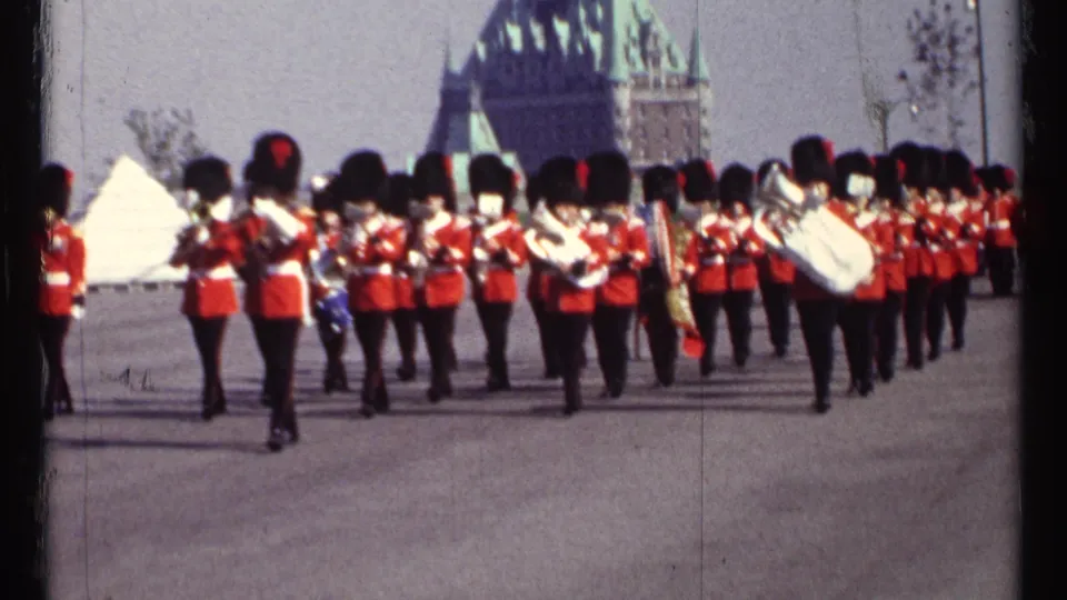 1967 Ottawa frame of uniformed band members marching across open pavement, filmed from a spectator viewpoint.