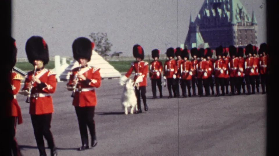 1967 Ottawa parade frame with RCMP musicians, a white ceremonial goat, and a long rank of red-uniformed personnel in the background.