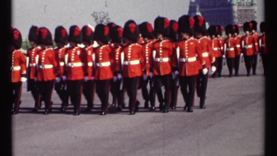 The 1967 Ottawa parade view tightens on the rear of the marching guard formation, with red tunics and black hats filling the frame.