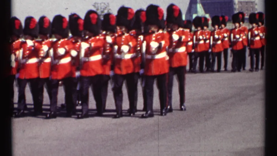 1967 Ottawa home-movie frame of Canadian Guards in red tunics and black bearskin hats marching in formation with rifles.