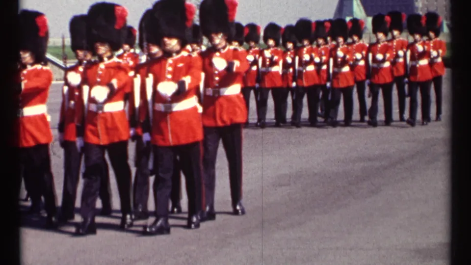 Close 1967 Ottawa frame of ceremonial guards marching past the camera in red tunics, bearskin hats, and white belts.