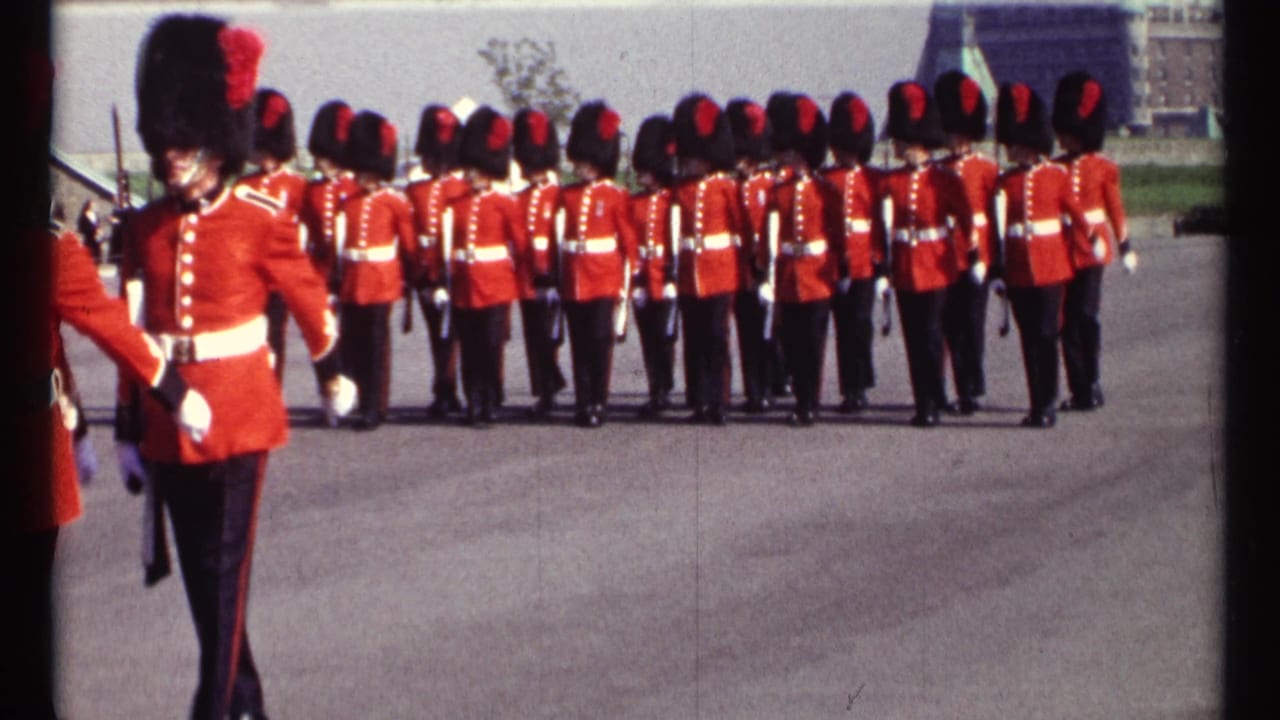 Uniformed guards in red tunics stand in formation on a paved parade ground.