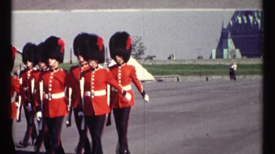 The 8mm frame catches guards passing close to the camera in Ottawa, with rifles, white belts, and distant Parliament Hill architecture visible.