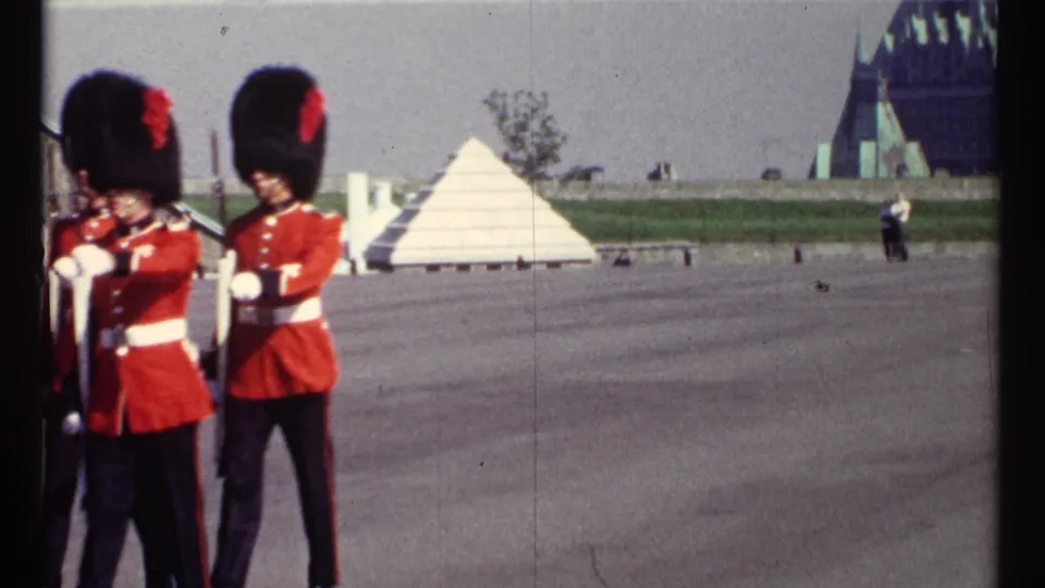 Two ceremonial guards remain at frame left while the open Ottawa parade ground, lawn, and distant buildings fill the background.