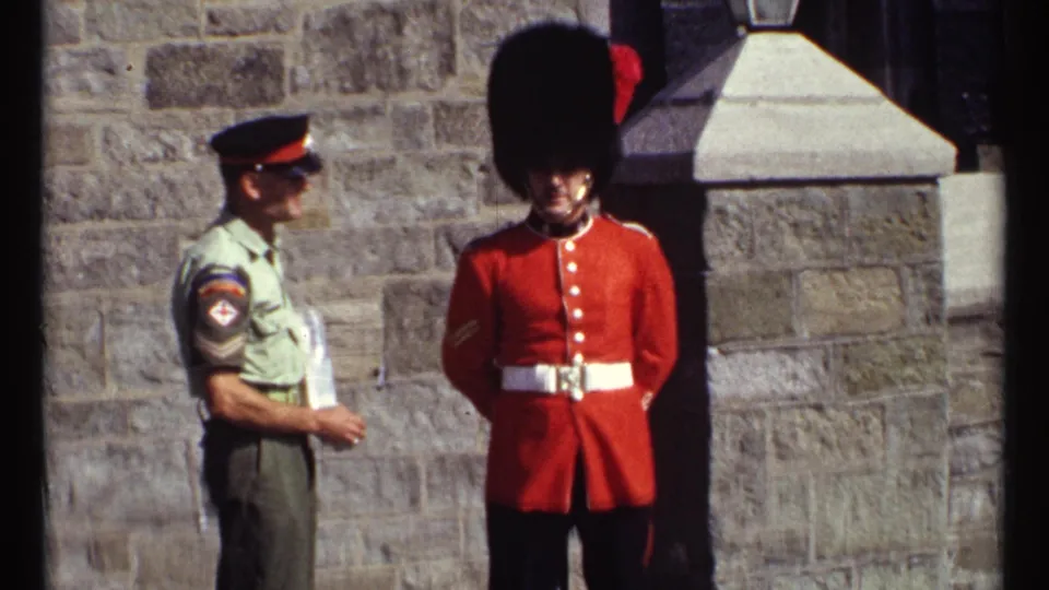1967 Ottawa frame showing a red-coated ceremonial guard facing forward while an officer stands nearby at a stone fortress wall.