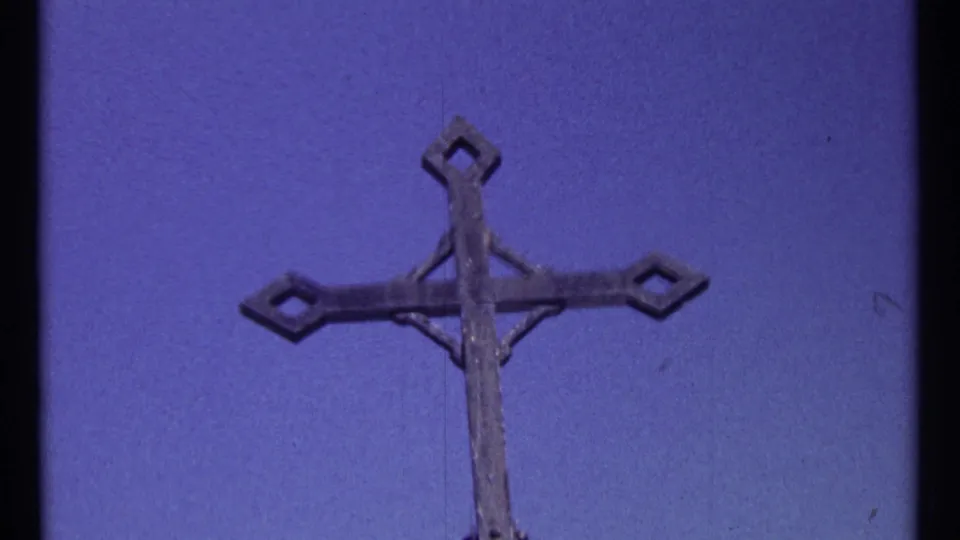 1967 Ottawa home-movie frame of a weathered cross top seen against blue sky with slight handheld softness.