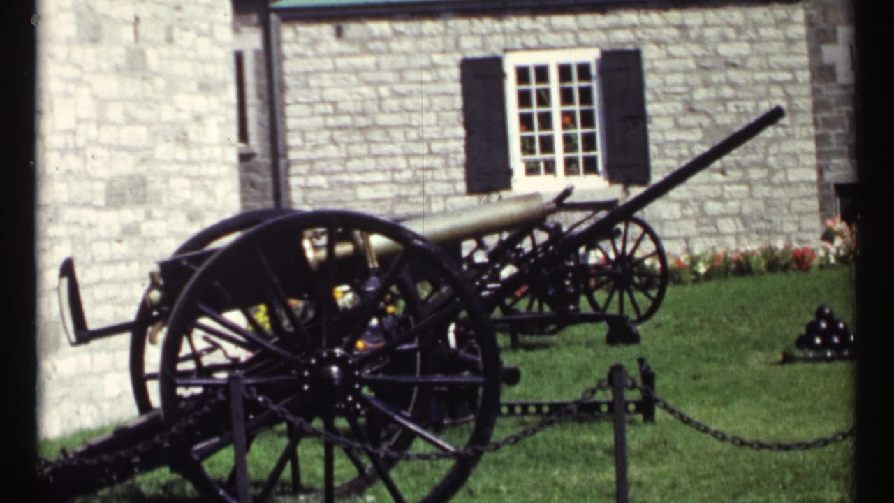 Historic cannons on a lawn in front of a stone building with black shutters.