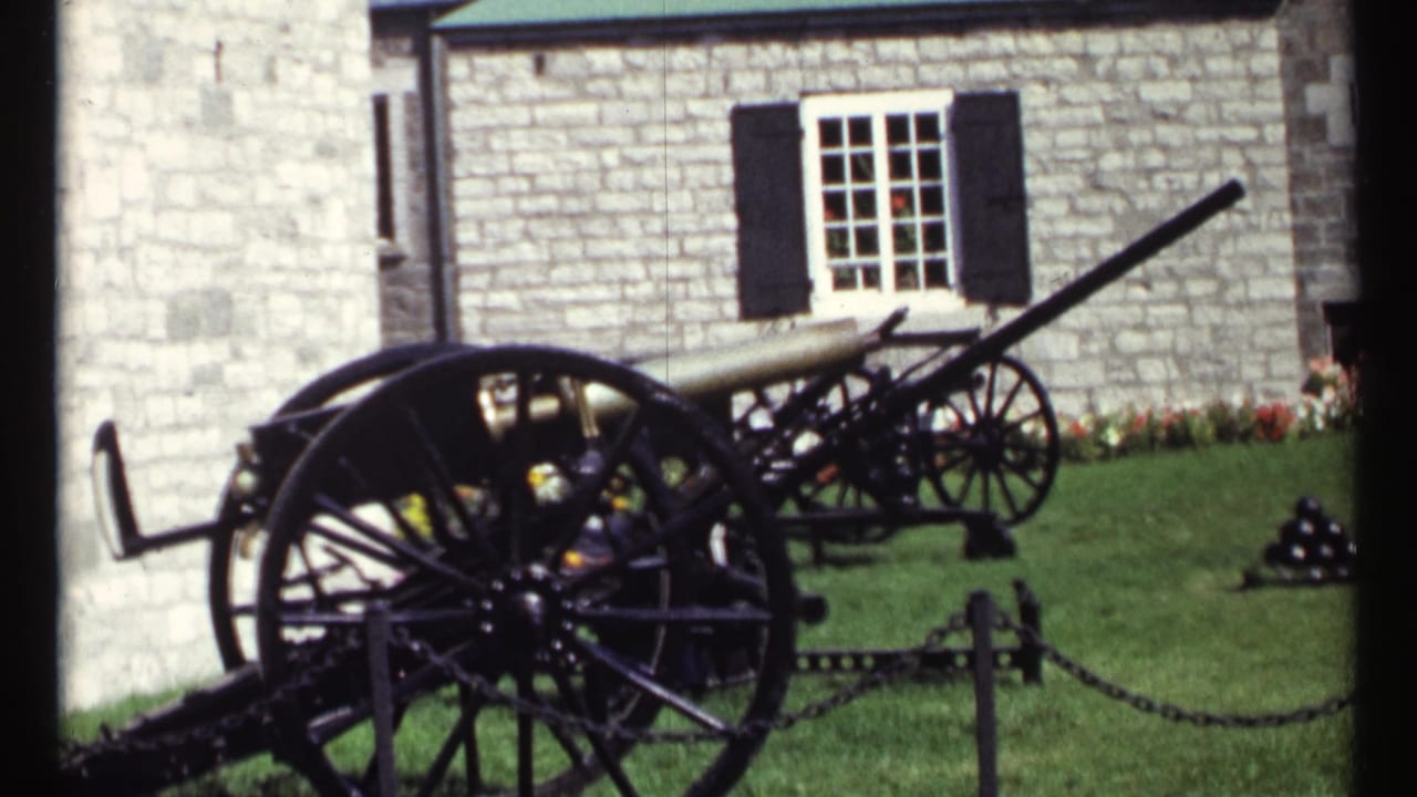 1967 Ottawa frame with cannon displays, chain posts, grass, flowers, and a stone facade with shuttered window.