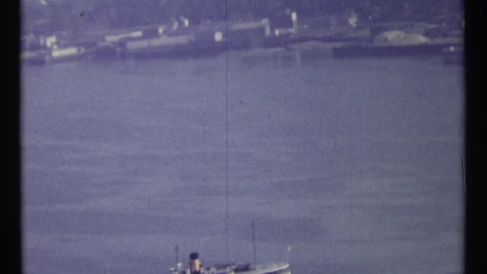 Faded 1967 Ottawa home-movie frame showing water, distant shore activity, and a large vessel seen from far away.