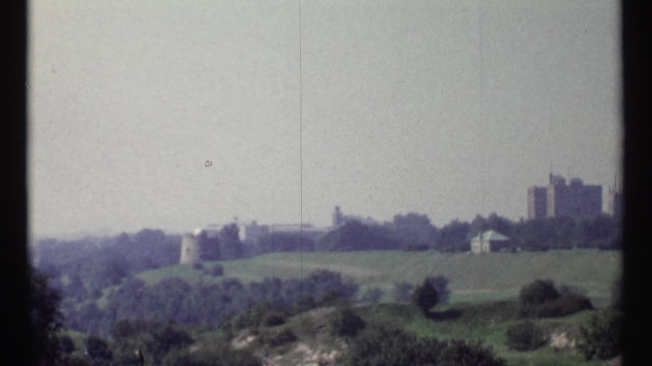 Green hillside with trees and distant buildings, including a castle-like structure.