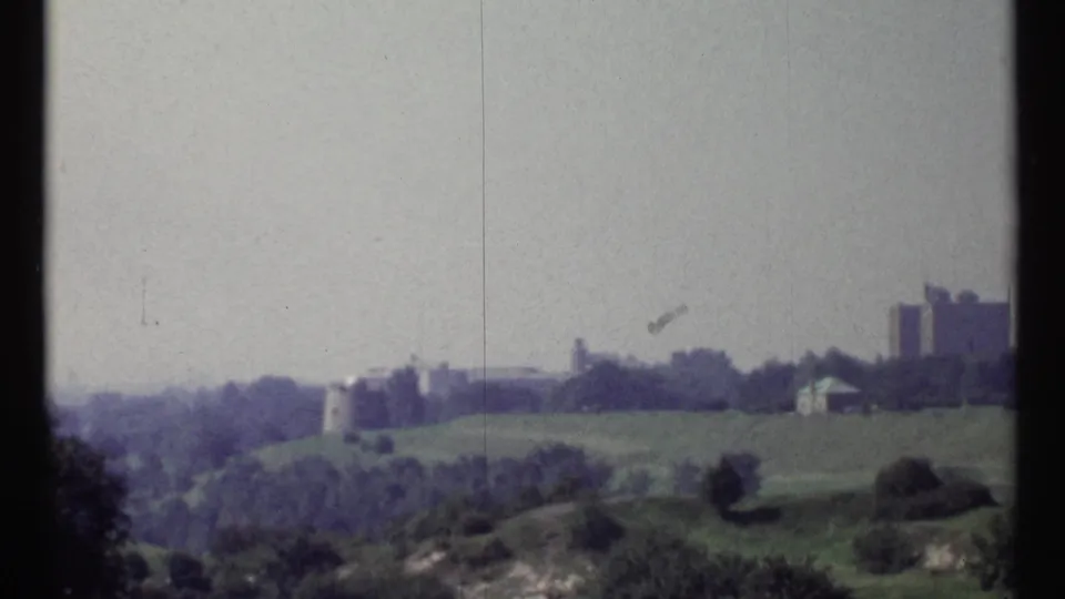 Wide 1967 Ottawa landscape frame with grassy slopes, tree cover, and distant buildings under a pale sky.