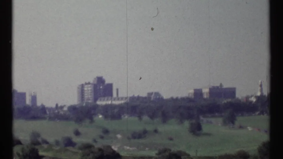 Faded 1967 Ottawa frame looking over open green ground toward distant buildings and skyline forms.