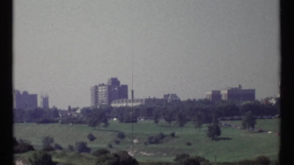 1967 Ottawa home-movie view of a green park with scattered trees and distant high-rise buildings under a hazy sky.