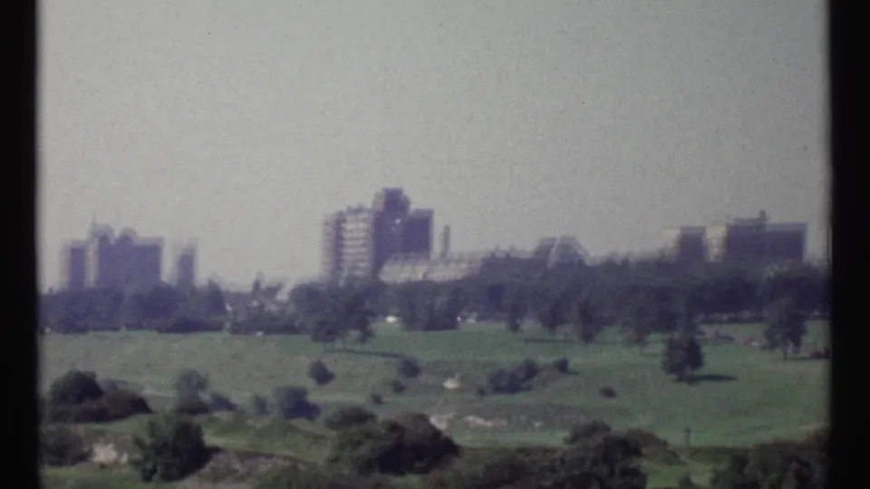 Soft 8mm frame showing Ottawa parkland, scattered trees, and distant mid-century buildings in 1967.
