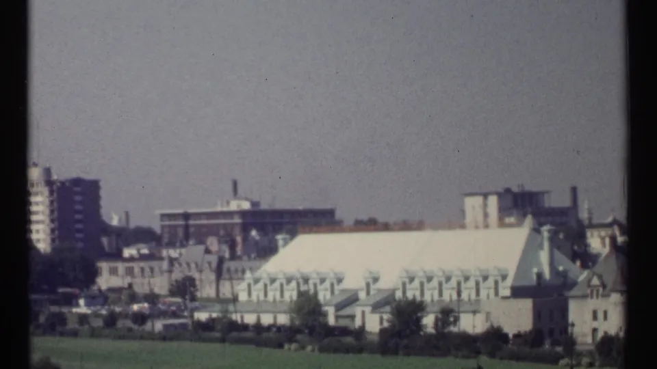 1967 Ottawa home-movie frame showing pale civic buildings with green copper roofs, trees, lawn, and distant high-rises.