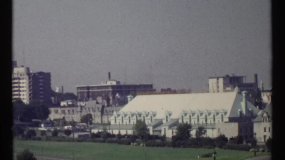 1967 Ottawa view across open grass toward green-roofed government buildings, trees, and mid-century high-rises.