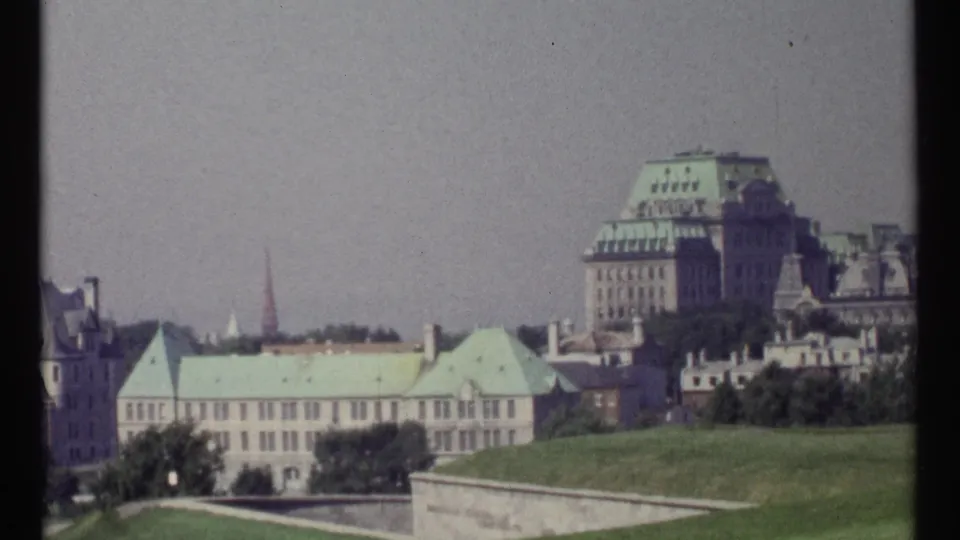 1967 Ottawa cityscape frame showing lawns, pale government-style buildings, green roofs, trees, and a tall background building.