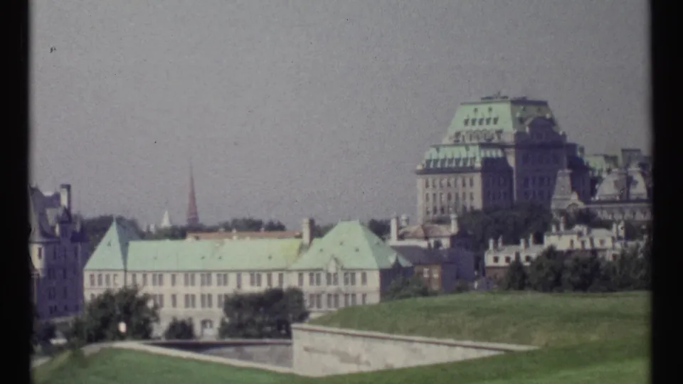 1967 8mm view of Ottawa civic architecture, green copper roofs, lawns, stone walls, trees, and hazy sky.