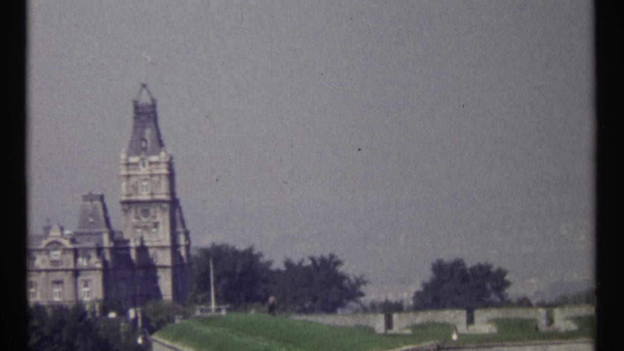 1967 Ottawa home-movie frame showing a tall stone tower, adjoining civic building, lawns, trees, and terrace walls.