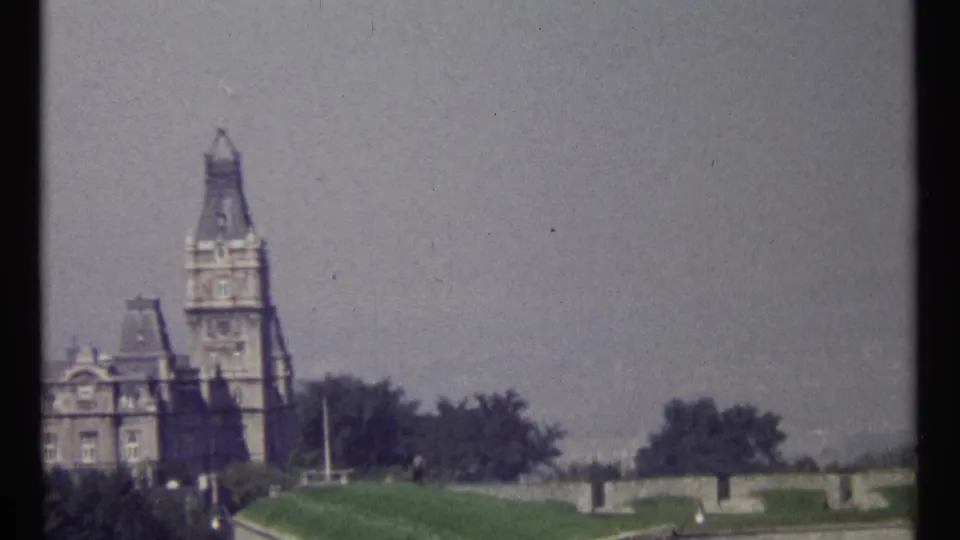 1967 Ottawa home-movie frame showing a tall stone tower, adjoining civic building, lawns, trees, and terrace walls.