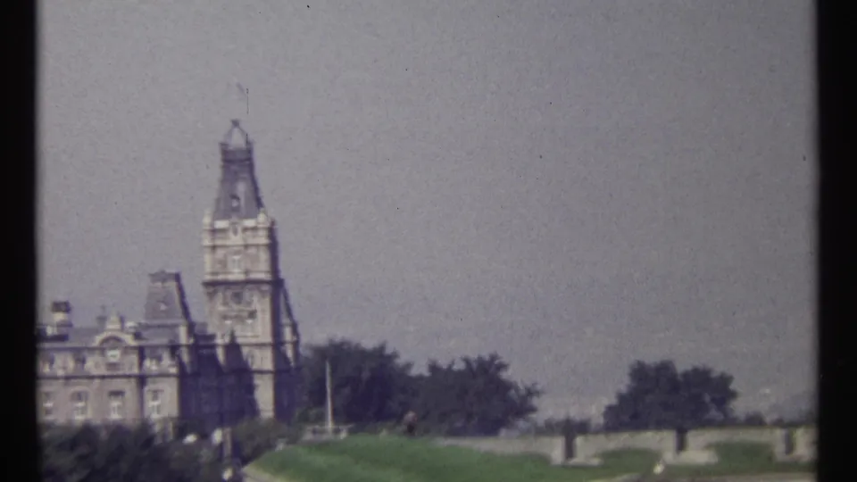 1967 Ottawa 8mm frame with a stone tower, historic building facade, lawn, trees, terrace wall, and soft film grain.