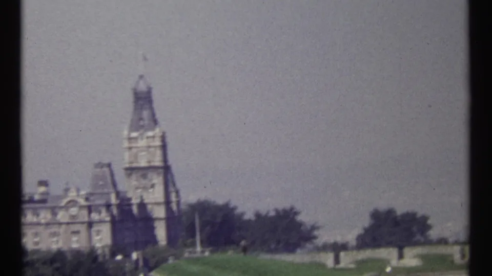 Late clip frame from 1967 Ottawa footage showing a tall stone tower, landscaped grounds, trees, and hazy sky.