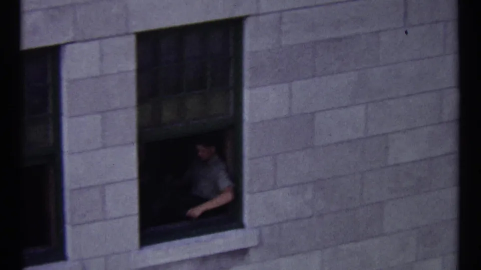 1967 Ottawa home-movie frame showing a man in a light shirt seated by an open window in a stone building.