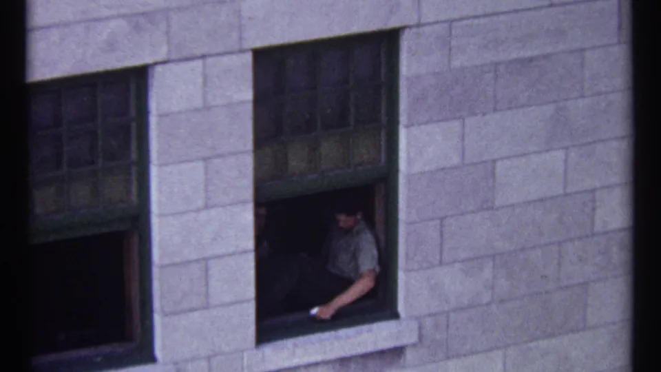 1967 Ottawa home-movie view of a man sitting by a dark open window in a stone building exterior.