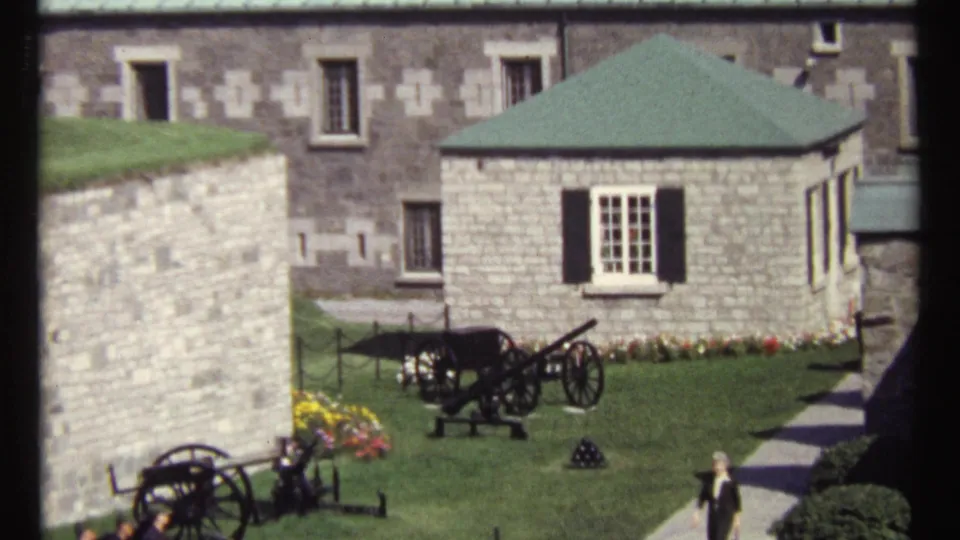 1967 Ottawa courtyard view with stone buildings, a green-roofed structure, display cannons, lawn, flowers, and visitors on a path.