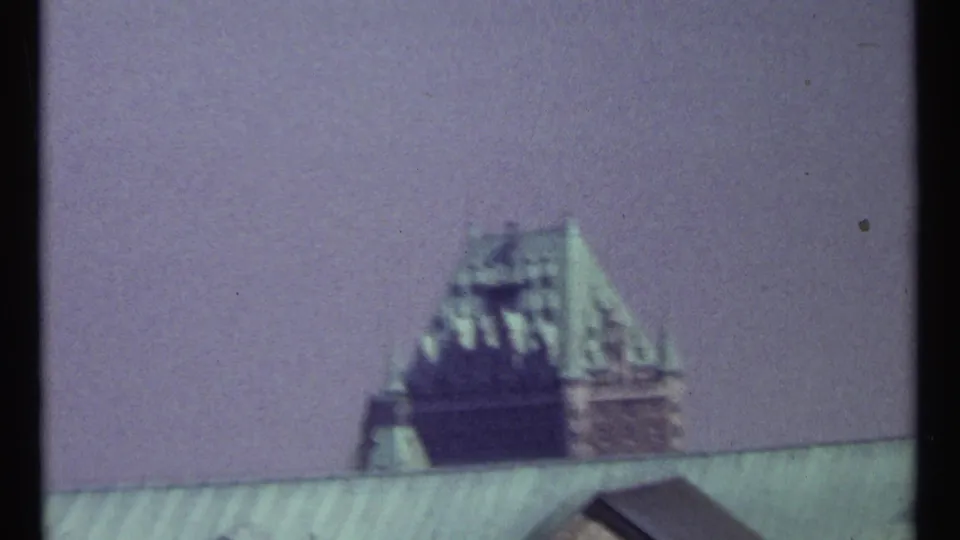 Soft 8mm view in Ottawa showing a distant château-style roof with green patina above a foreground roofline and pale sky.