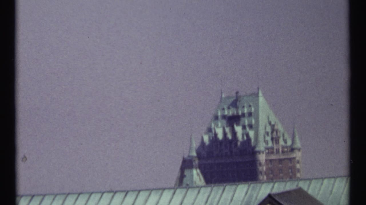 Distant turreted building behind a long green roof, framed by dark 8mm film edges.