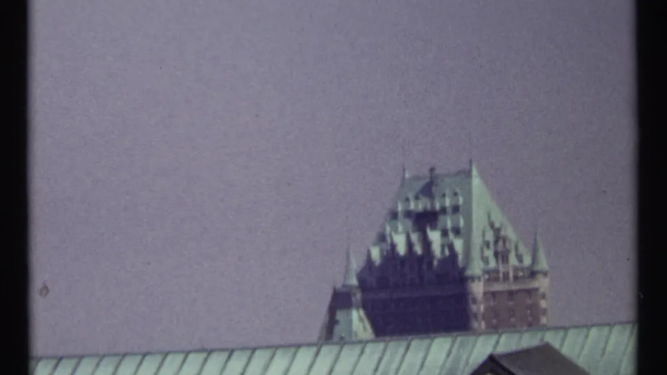 A 1967 8mm view of a distant château-style landmark behind rooftops, with muted color and dark film borders.