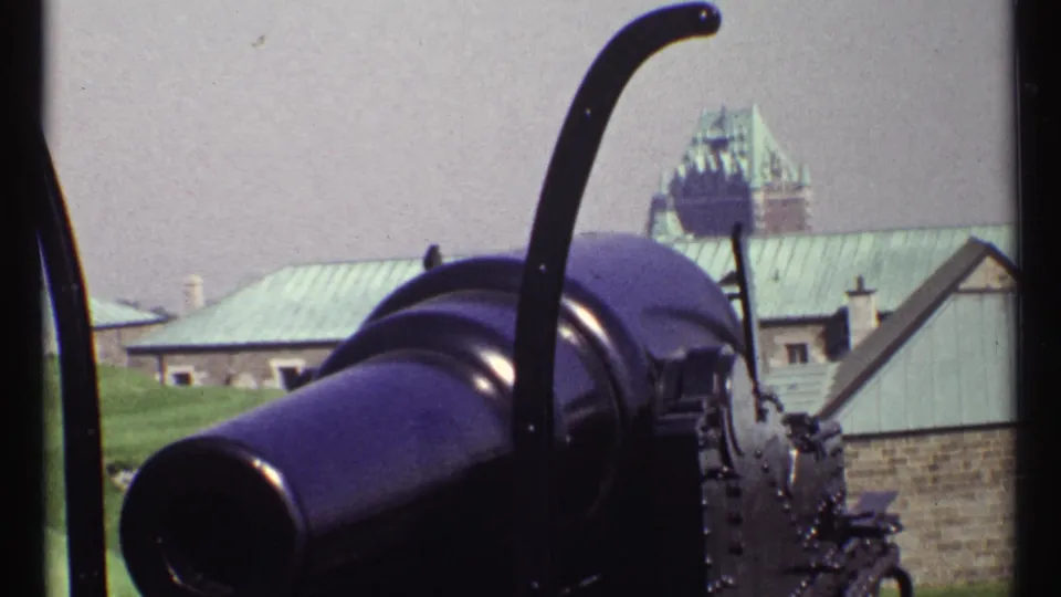 A 1967 8mm frame shows a historic cannon in front of stonework, with the distant château-style landmark and green roofs behind it.