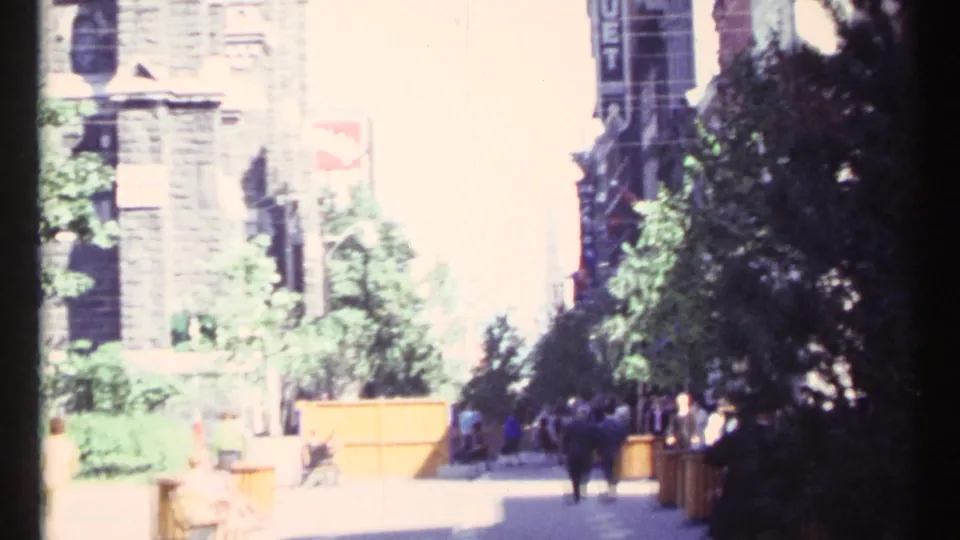 Overexposed 1967 Ottawa street frame showing pedestrians, trees, planters, stone building frontage, and a vertical hotel sign.