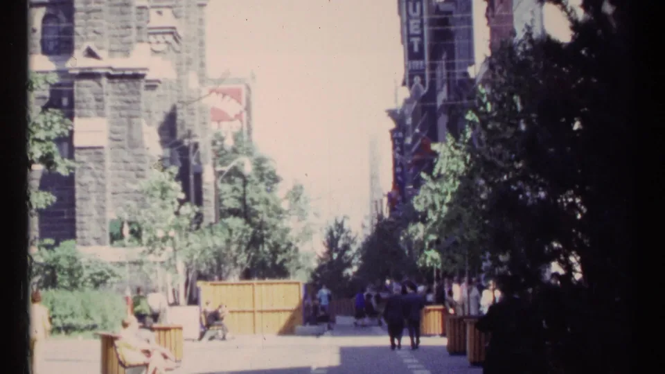 1967 Ottawa street view with pedestrians near benches, trees, stone architecture, a wooden barrier, and a vertical sign.