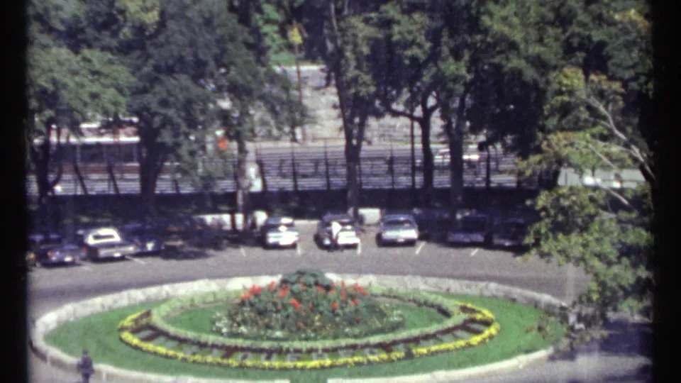 Elevated 1967 Ottawa view of a circular flower bed bordered by parked cars, trees, and shaded roadway.