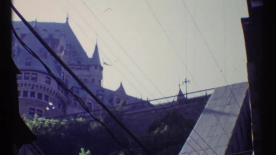 1967 Ottawa home-movie view toward a turreted historic building, with overhead wires and rooflines crossing the frame.