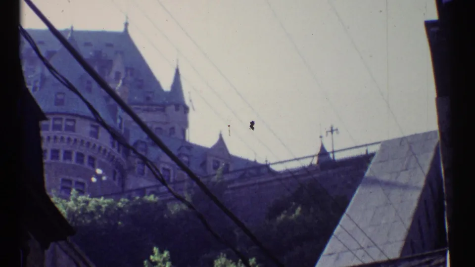 Ottawa 1967 home-movie frame showing a historic turreted building beyond rooftops, crossed by overhead utility lines.