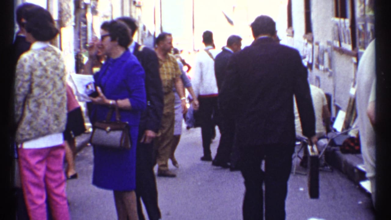 Pedestrians walk and stand in a narrow shopping walkway with storefronts.
