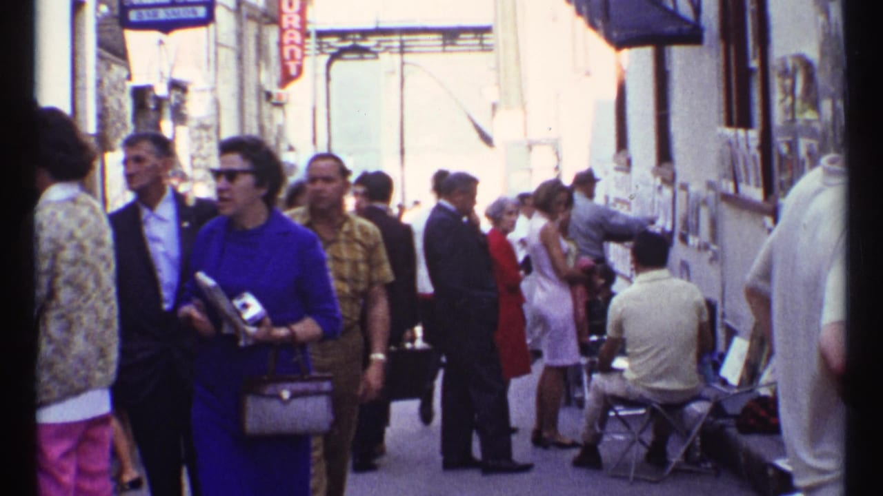 Crowded narrow street with pedestrians, shop signs, wall displays, and a seated street guitarist.