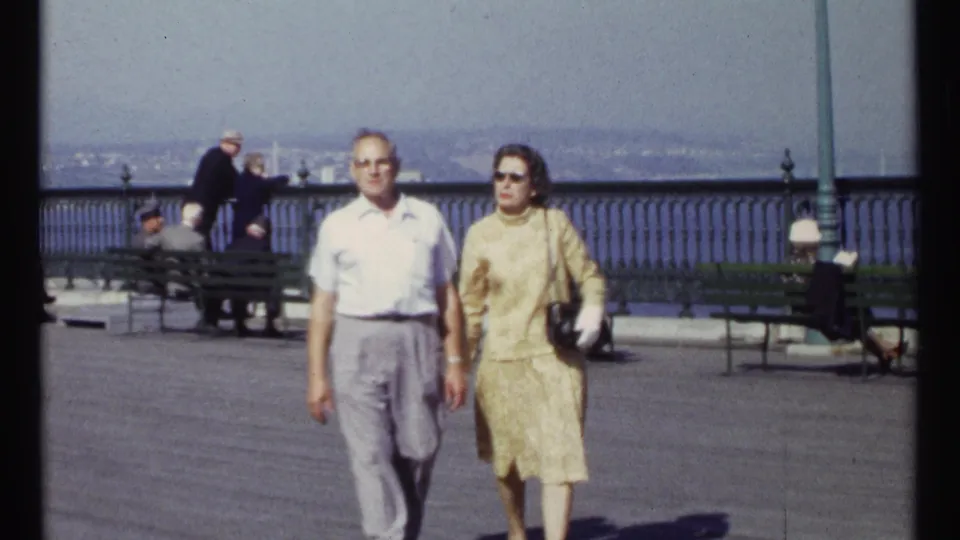 In the Ottawa 1967 home-movie frame, the couple is closer in view as background adults sit near the waterfront railing.