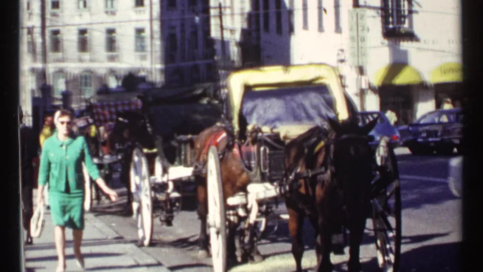 A pedestrian in green walks beside horse-drawn buggies and cars in 1967 Ottawa, with bright awnings and stone buildings visible.