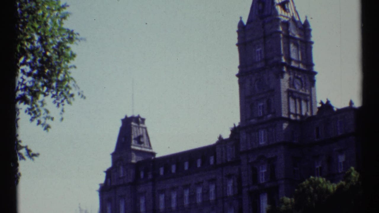 Château Laurier tower and roofline seen beyond leafy trees under a pale sky.