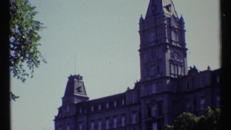 Soft 8mm frame of Château Laurier in Ottawa, with ornate stonework, tower forms, trees, and visible film borders.