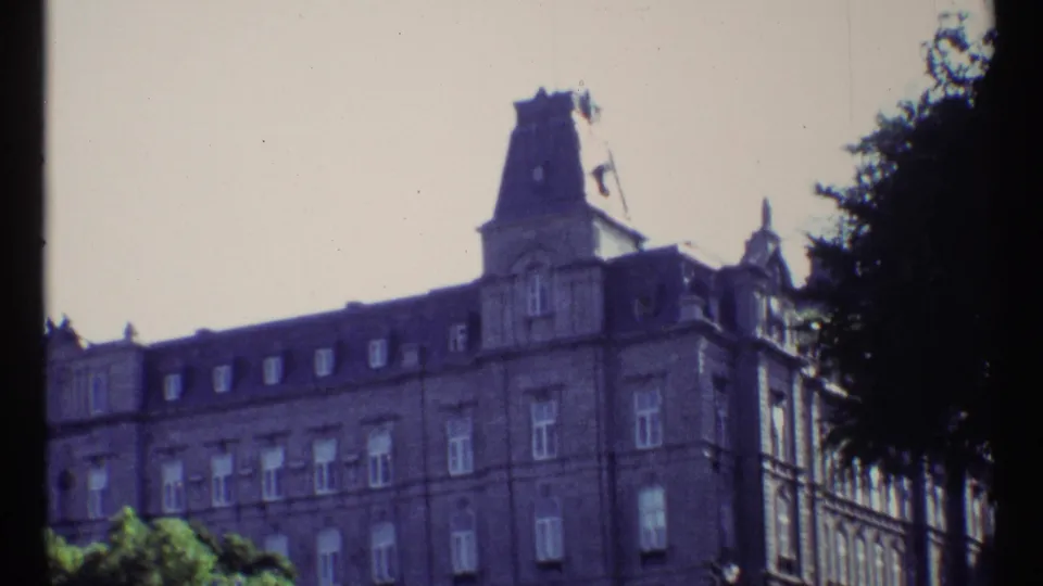 1967 Ottawa home-movie frame widening to show more of the stone facade, a tower above the roof, rows of windows, trees, and a bright sky.