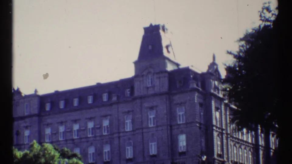 Ottawa 1967 home-movie frame showing a grand stone building with dormer windows, a tower, and tree shadows at the edge.