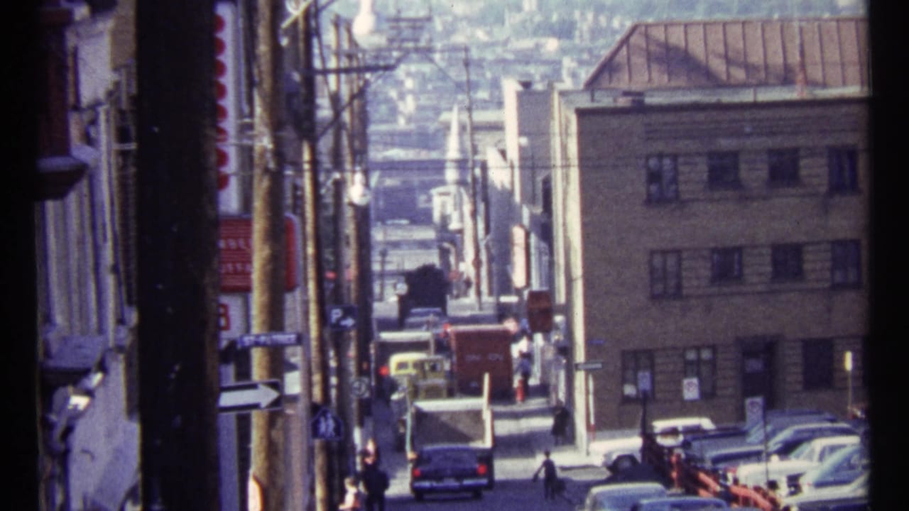 1967 Ottawa street view looking downhill past low-rise buildings, older cars, pedestrians, overhead wires, and utility poles.