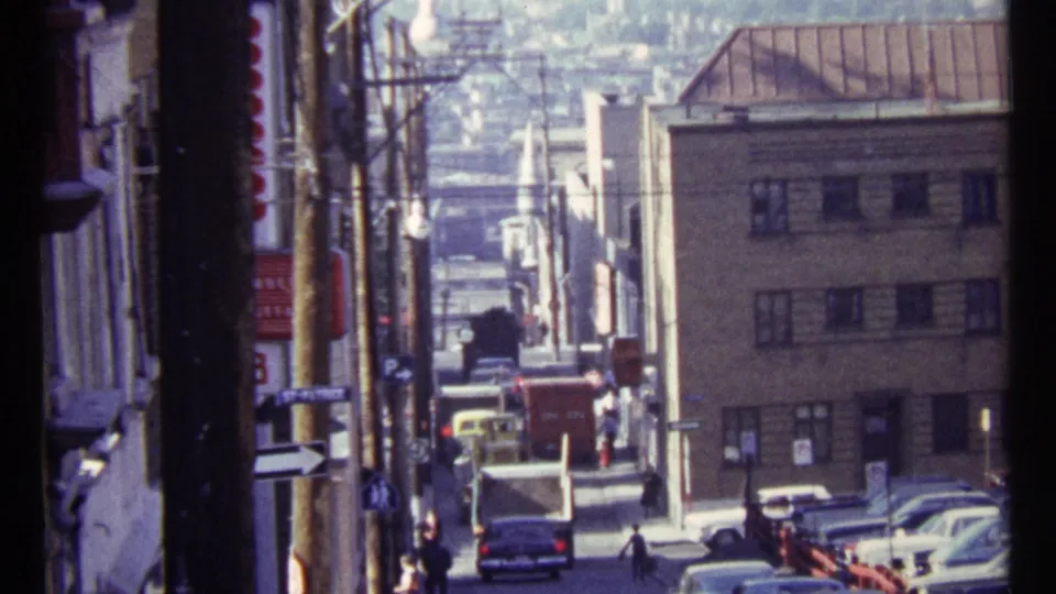 1967 Ottawa street view looking downhill past low-rise buildings, older cars, pedestrians, overhead wires, and utility poles.